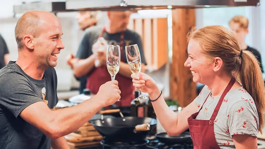 Two colleagues cooking together + enjoying a glass of red wine